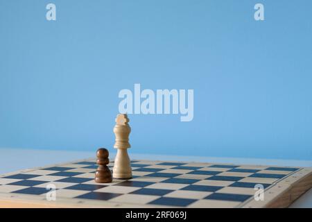 Weißer Schachkönig und schwarzer Bauer auf einem Schachbrett auf hellblauem Hintergrund Stockfoto