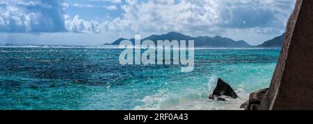 Felsen auf La Digue Island, Seychellen mit Praslin Island im Hintergrund über der Bucht. Stockfoto