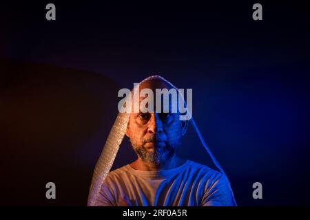 Glatzkopf mit Bart und Luftpolsterfolie um den Kopf. Isoliert auf dunkelrotem Hintergrund. Stockfoto