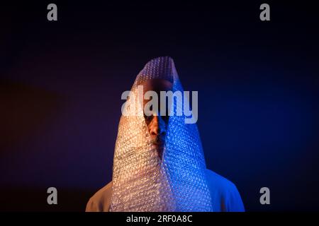 Glatzkopf mit Bart und Luftpolsterfolie um den Kopf. Isoliert auf dunkelrotem Hintergrund. Stockfoto