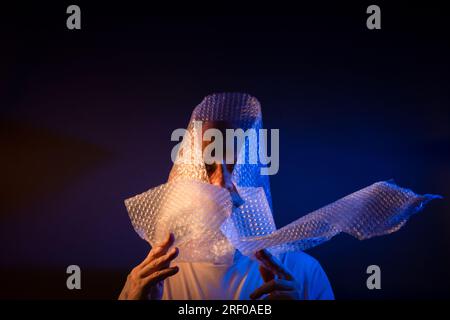 Glatzkopf mit Bart und Luftpolsterfolie um den Kopf. Isoliert auf dunkelrotem Hintergrund. Stockfoto