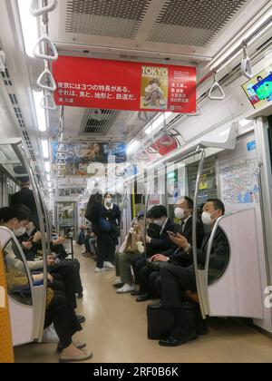 Japanische Geschäftsleute und Pendler, einige tragen Gesichtsmasken, sitzen in einer Zugkutsche des U-Bahn-/U-Bahn-Systems Tokio. Stockfoto