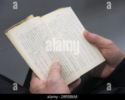 Nahaufnahme des japanischen Schriftzugs auf der Seite eines kleinen Buches, das ein Pendler in der U-Bahn in Tokio in zwei Händen hielt. Stockfoto