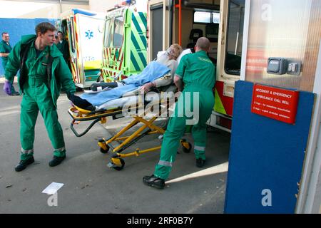Sanitäter bringen einen Patienten auf einer Liege in einen Krankenwagen vor einer Notaufnahme. Stockfoto