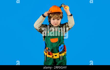 Kinderwerkstatt in Bauernuniform mit Werkzeuggürtel und Hammer. Kleiner Junge mit Schutzhelm und Overall mit Hammer. Baumeister im Schutzhelm Stockfoto