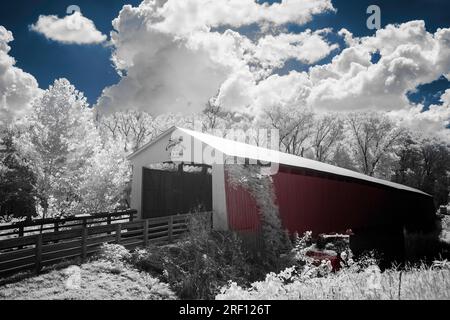 Ein farbiges Schwarzweißbild einer roten überdachten Brücke in der Nähe von Shieldstown, IN. Weißes Laub mit blauem Himmel, roter Seitenwand und rotem Wasser. Stockfoto