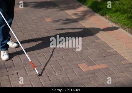 Eine gesichtslose blinde Frau läuft mit einem Stock die Straße entlang. Stockfoto