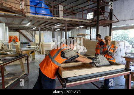 Antakya, Türkei. 18. Juli 2023. Im Rahmen des Projekts „Yuva“ (Nest) bauen Freiwillige im Bezirk Samandag ökologische Holzhäuser, die Unternehmen oder Privatpersonen über eine Partnerorganisation an Erdbebenopfer spenden können. Das Projekt „Yuva“ (Nest) beschäftigt 15 Frauen und 15 Männer aus der Region, die selbst vom Erdbeben betroffen sind. Notunterkünfte in der Hitze und den Schutt - sechs Monate nach den Erdbeben im Südosten der Türkei am 6. Februar leiden die Menschen noch immer unter den Folgen. Kredit: Bradley Secker/dpa/Alamy Live News Stockfoto