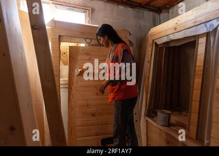 Antakya, Türkei. 18. Juli 2023. Im Rahmen des Projekts „Yuva“ (Nest) bauen Freiwillige im Bezirk Samandag ökologische Holzhäuser, die Unternehmen oder Privatpersonen über eine Partnerorganisation an Erdbebenopfer spenden können. Das Projekt „Yuva“ (Nest) beschäftigt 15 Frauen und 15 Männer aus der Region, die selbst vom Erdbeben betroffen sind. Notunterkünfte in der Hitze und den Schutt - sechs Monate nach den Erdbeben im Südosten der Türkei am 6. Februar leiden die Menschen noch immer unter den Folgen. Kredit: Bradley Secker/dpa/Alamy Live News Stockfoto