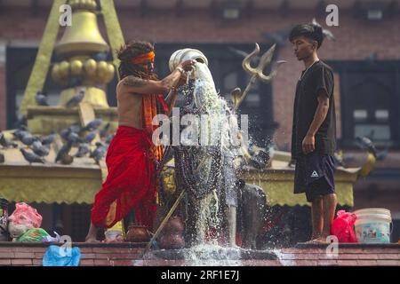 Ein hinduistischer Priester gießt Milch ein, während er Idol von Lord Shiva am Montag, den 31. Juli 2023, im Shiva-Tempel in Kathmandu, Nepal betet. Der heilige Monat Stockfoto