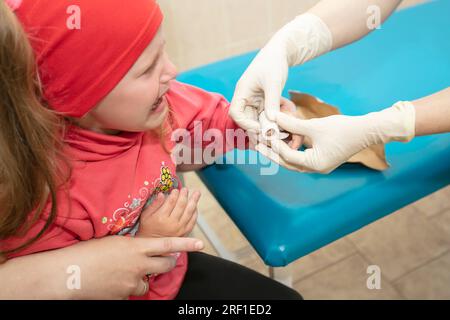 Die Hände des Arztes verbinden den schmerzenden Finger mit einem Verband des Kindes. Verletzung und Wunde am Finger bei Kindern Stockfoto