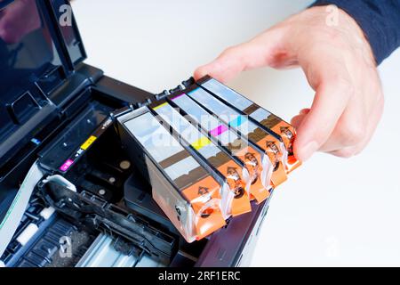 Die Hand nimmt eine der frischen Tintenpatronen, die in einem neuen Tintenstrahldrucker eingesetzt wurden. Austausch von Verbrauchsmaterialien. Stockfoto