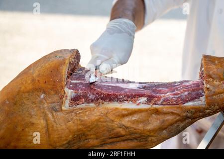 Professioneller Koch, der iberico-spanischen Schweineschinken am Partytisch des Restaurants schneidet Stockfoto