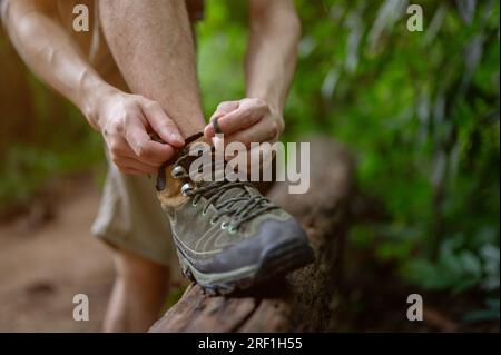 Nahaufnahme eines Wanderer, der seine Schnürsenkel bindet, während er im grünen Wald wandert. Bergwanderung, Sommeraktivitäten, Naturerlebnisse Stockfoto