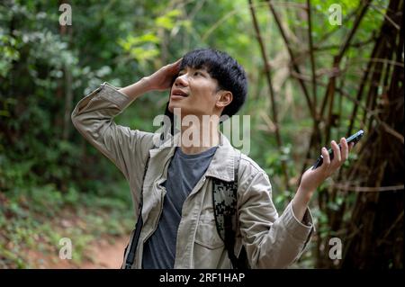 Ein verwirrter und verwirrter männlicher asiatischer Reisender mit seinem Smartphone verirrt sich im Wald, während er alleine wandert. Stockfoto