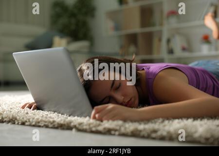 Müde Frau, die nachts zu Hause über einem Laptop auf dem Boden schläft Stockfoto