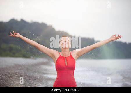 Eine glückliche Frau mittleren Alters am Strand hob ihre Hände und genießt einen glücklichen Moment. Stockfoto