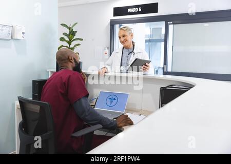 Verschiedene männliche und weibliche Arzte diskutieren Arbeit und setzen Tablet in der Rezeption des Krankenhauses ein Stockfoto