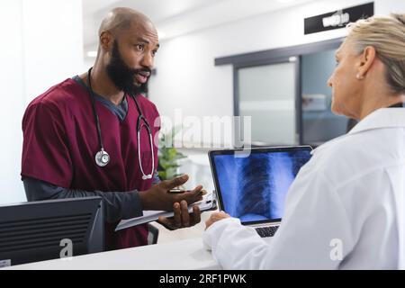 Verschiedene männliche und weibliche Ärzte diskutieren über Arbeit und verwenden Laptop in der Rezeption des Krankenhauses Stockfoto