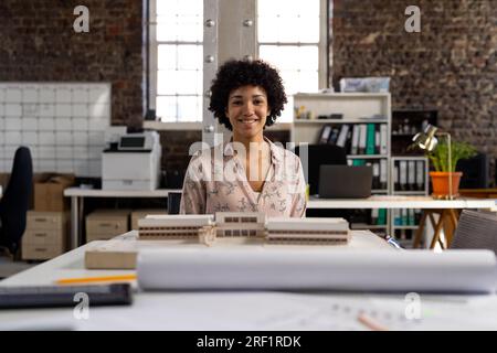 Porträt einer glücklichen birassischen Architektin, die am Schreibtisch sitzt, mit einem Baumodell im Büro Stockfoto
