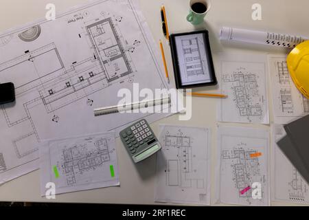 Blick von oben auf den Schreibtisch mit architektonischen Bauplänen, Tablet, Kaffee und Schutzhelm Stockfoto