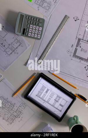 Blick von oben auf den Schreibtisch mit architektonischen Bauplänen, Tablet, Taschenrechner, Lineal, Bleistiften und Kaffee Stockfoto