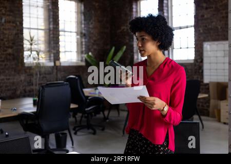 Birassische Geschäftsfrau, die sich auf einem Smartphone unterhält und Dokumente im Büro hat Stockfoto