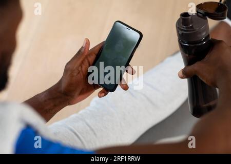 Hände eines afroamerikanischen Mannes, der auf der Matte sitzt und sein Smartphone zu Hause benutzt Stockfoto