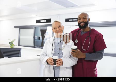 Portrait von glücklichen, vielfältigen männlichen und weiblichen Ärzten, die Take-away-Kaffee in der Rezeption im Krankenhaus halten Stockfoto