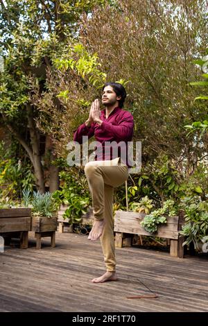 Fokussierter indischer Mann, der Yoga auf der sonnigen Terrasse praktiziert Stockfoto