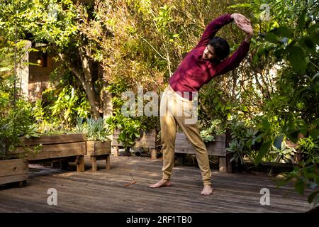 Fokussierter indischer Mann, der Yoga auf der sonnigen Terrasse praktiziert Stockfoto