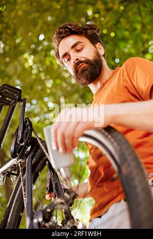 Detaillierte Aufnahme der modernen Fahrradkette, die sorgfältig mit Fett geschmiert wird, für sichere Outdoor-Freizeit. Die Abbildung zeigt, wie der Scheibenbremsring des Motorrads von einem männlichen Radfahrer im Sommer geschmiert wird Stockfoto
