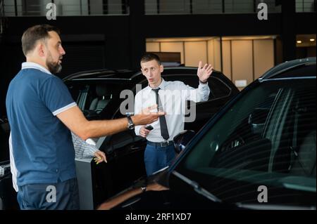 Der Verkäufer demonstriert den Käufern das Fahrzeuginnere. Ein weißes Paar sucht sich ein Auto aus. Stockfoto