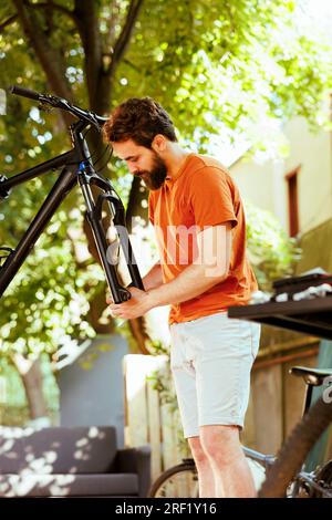 Lebhafter junger Kaukasier, der das Headset und den Lenker im Hof des Fahrrads anpasst und sichert. Zerlegtes Fahrrad wird draußen von sportliebenden Männchen für Sommerradfahren repariert. Stockfoto