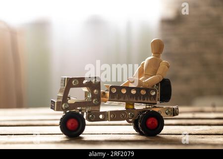 Ein kleiner Mann aus Holz sitzt auf einer Schiene aus Metallklötzen auf einem Holzbrett, Kinderspielzeug und Transportmitteln Stockfoto