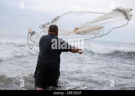 Ein Fischer wirft ein Fischernetz ins Meer. Stockfoto