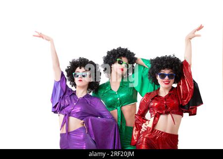Drei Mädchen im Disco-Stil in bunten Kostümen und schwarzen Perücken auf weißem Hintergrund. Stockfoto