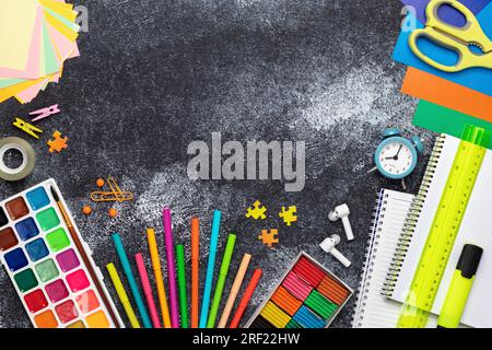 Schulbedarf auf einem schwarzen Brett. Büropapier an der Tafel. Notizbuch, Stift, Wecker, Schere, Lineal, Plastin, farbiges Papier Stockfoto