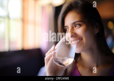 Glückliche Frau, die Wasser aus durchsichtigem Glas trinkt, schaut auf die Seite in einem Restaurant Stockfoto