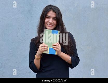 Foto einer hübschen indischen Studentin, die ein Buch in der Hand hält und in die Kamera schaut. Stockfoto