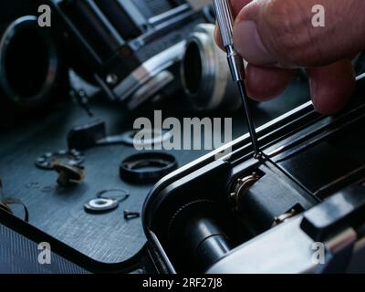 Nahaufnahme der Hand mit einem Schraubenzieher, der eine alte Filmkamera repariert. Stockfoto