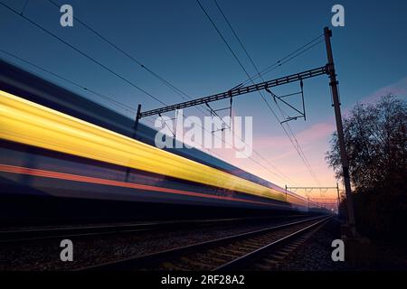 Eisenbahn bei Sonnenaufgang. Lange Zugbelastung auf Eisenbahngleisen. Moderner Intercity-Personenzug. Stockfoto