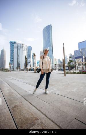 Junge Frau steht vor Wolkenkratzern in Doha Stockfoto