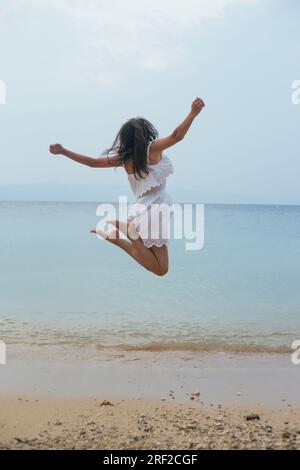 Junge Frau in weißem Sommerkleid, die am Strand sprang Stockfoto