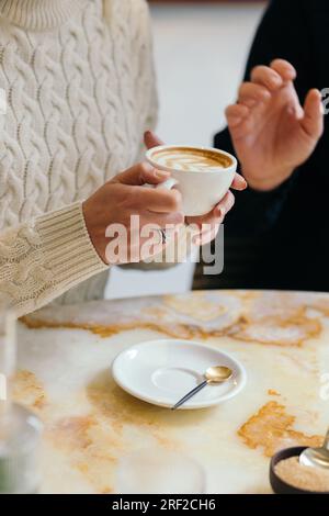 Weibliche Hände halten eine Tasse Cappuccino Stockfoto
