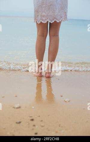 Weibliche Beine stehen am Sandstrand Stockfoto