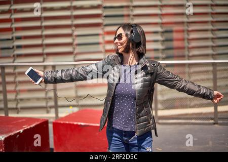 Lächelnde Frau, die Musik hört und auf der Straße tanzt Stockfoto