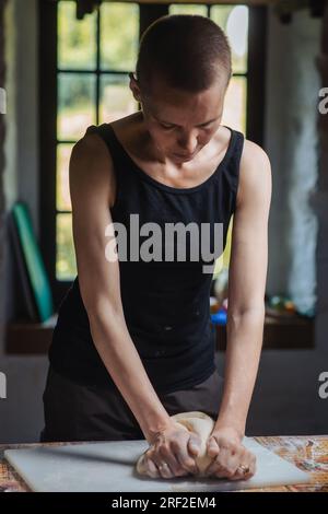 Kahlköpfige Frau, die in der Küche Teig knete. Brot machen. Stockfoto