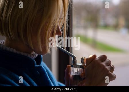 Eine Frau raucht Marihuana, Cannabis. Eine Erwachsene Frau mit blonden Haaren zündet ein Rauchergerät an. Entspannung, ärztliche Verschreibung. Stockfoto