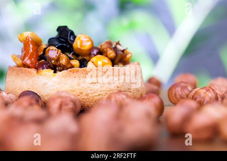 Weizentörtchen mit süßer Füllung, knusprige Törtchen mit Haselnüssen, Erdnüssen und anderen Zutaten, Weizenteig Törtchen mit Nüssen und getrockneten Früchten in Crea Stockfoto